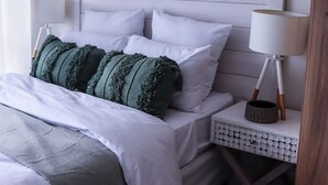 Ein ordentlich bezogenes Bett mit weißer und grüner Bettwäsche, eine Nachttischlampe und ein gerahmtes Landschaftsbild an der Wand.