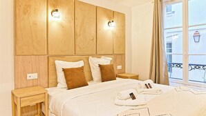 A hotel room with a large bed, two bedside tables, a headboard with wall sconces, and a window with a view of the city. - Magnificent air-conditioned flat Galeries Lafayette (Paris)