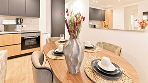 A modern dining area with a round table set for four, a vase with red flowers, and a kitchen in the background. - Magnificent air-conditioned flat Galeries Lafayette (Paris)
