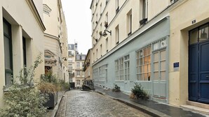 A narrow cobblestone street flanked by buildings with large windows and a blue door on the right. - Magnificent air-conditioned flat Galeries Lafayette (Paris)