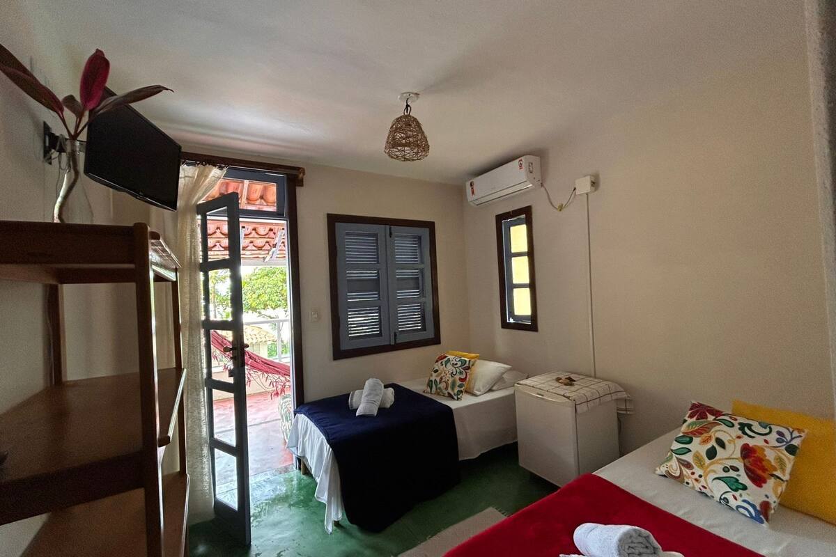 Ein Zimmer mit einem Bett, einem Schreibtisch, einem Stuhl, einem Fenster mit Rollläden, einem Deckenventilator und einer Klimaanlage.