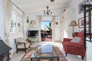 A living room with a TV, a glass coffee table, a red armchair, and a view to the outside.