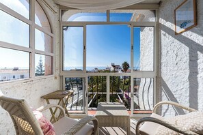 A balcony with wicker furniture, a view of the sea, and a white textured wall.