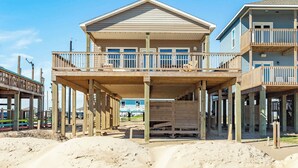 Une maison de plage à deux étages, dotée d’un balcon au premier étage et d’une véranda couverte.