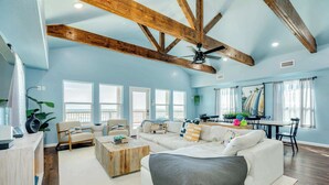 Un salon spacieux avec un plafond haut, des poutres en bois, un ventilateur de plafond et une grande fenêtre.