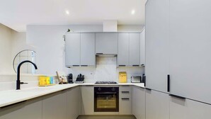 A modern kitchen with grey cabinets, a white countertop, a black faucet, and a wooden floor. - Elegant Two-Bedroom Piccadilly Circus Apartment (Greater London)