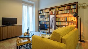 A living room with a sofa, a bookshelf, a television, and a table with a chessboard.