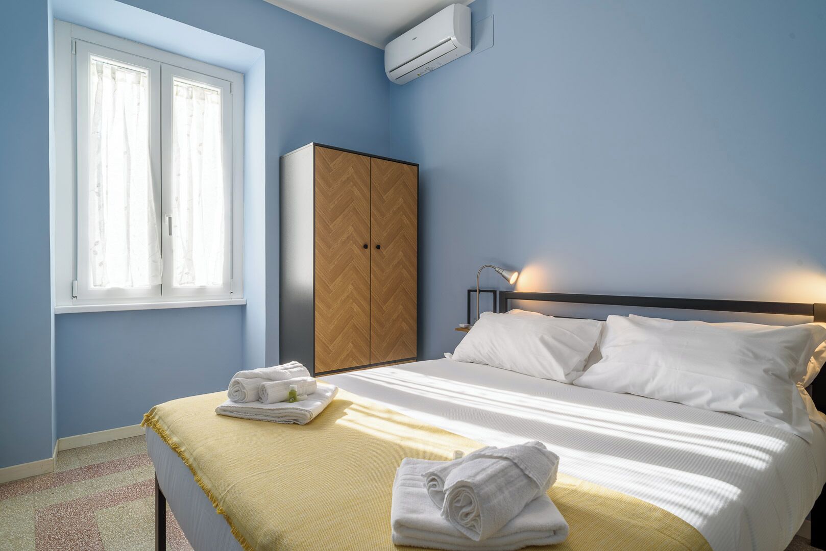 A bedroom with a bed, a wardrobe, a window, and an air conditioning unit.