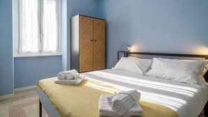 A bedroom with a bed, a wardrobe, a window, and an air conditioning unit.