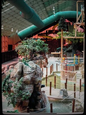 En inomhusbadpark med klippformationer, ett vattenfall och en lekplats.