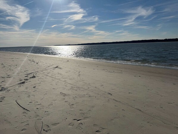 A beach with footprints and tire tracks in the sand, leading to the water.