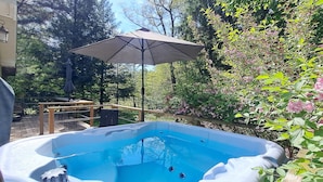 Un jacuzzi en un jardín con terraza de madera y un pérgola con sombrilla.