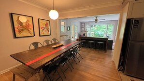 Una cocina moderna con una mesa de comedor de madera, sillas negras y una franja roja. Hay un refrigerador, un ventilador de techo y una ventana con vistas a zonas verdes.