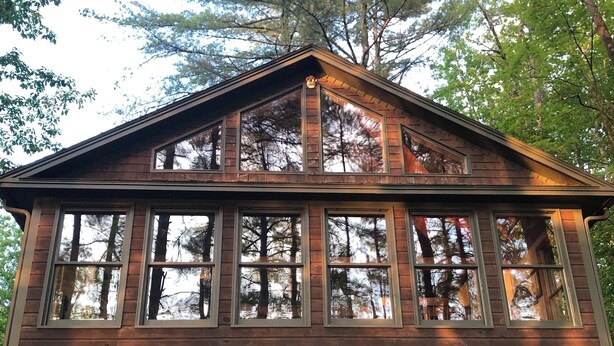 Eine Holzhütte mit großen Fenstern, einer Veranda und einem Felsengarten mit rosa Blumen.