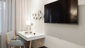 A modern room with a white desk, a chair, a bench, a TV, and a window with curtains. - SQUARE Elegant Suite II on Aristotelous Square (Thessaloniki)