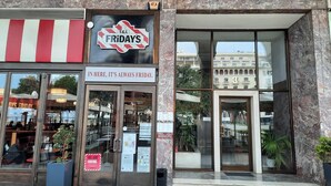 A storefront with a sign reading "T.G.I. Fridays" and a slogan "IN HERE, IT'S ALWAYS FRIDAY." - SQUARE Elegant Suite II on Aristotelous Square (Thessaloniki)