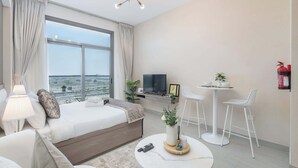 A modern hotel room with a large window, a bed, a TV, a small dining area, and a fire extinguisher. - StayShort - Inviting studio in Laya Heights (Dubai Studio City)
