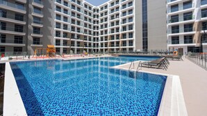A modern hotel with a central swimming pool, multiple balconies, and a children's play area. - StayShort - Inviting studio in Laya Heights (Dubai Studio City)