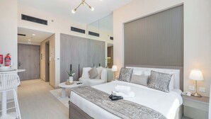 A modern hotel room with a large bed, bedside tables, a small desk, and a mirror. - StayShort - Inviting studio in Laya Heights (Dubai Studio City)
