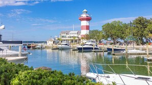 A marina with boats docked, a lighthouse, and a building with a balcony overlooking the water. - 2 BDR w/Water Views, Beach Access, & Shared Pool! (Hilton Head Island)