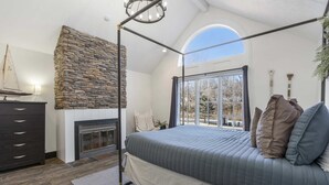 A bedroom with a stone wall, a fireplace, a four-poster bed, and a large window. - Foggy River Retreat – For 16! (Hollister)
