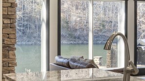 A kitchen with a stone countertop, a sink, and a window overlooking a lake with trees. - Foggy River Retreat – For 16! (Hollister)