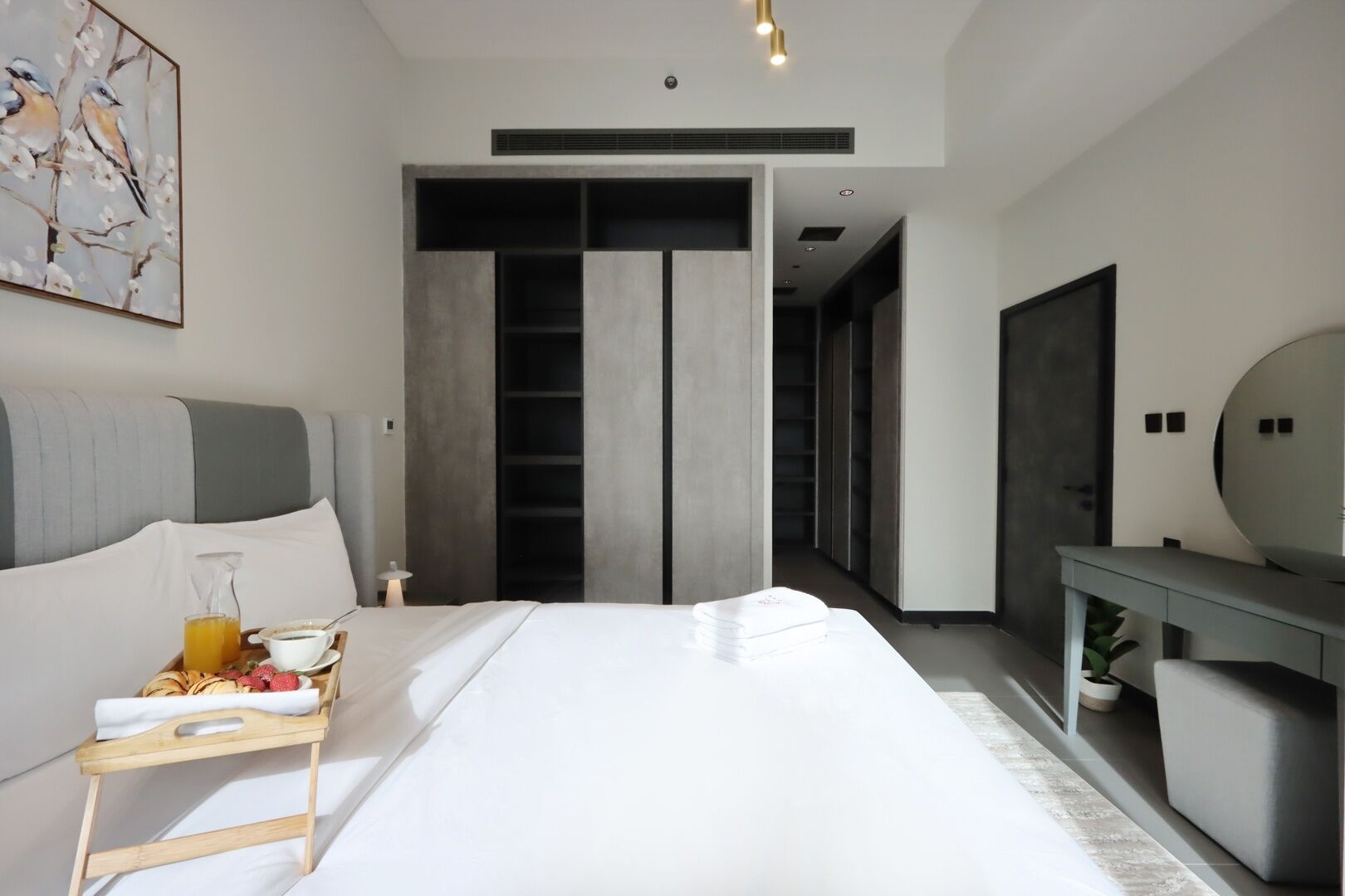 Et moderne hotelværelse med en stor seng, et natbord med et morgenmadssæt, et stort spejl og en garderobe.