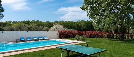 Piscina con sillas de descanso y una mesa de ping-pong en un patio cubierto de césped.