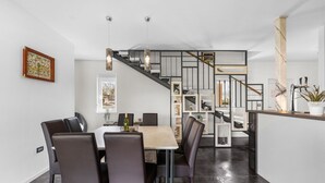 A modern dining area with a wooden table and chairs, a staircase with a geometric railing, and a potted plant on the counter.
