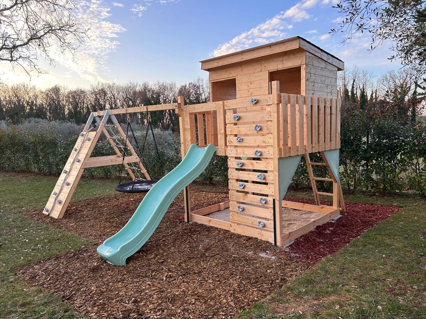 Eine hölzerne Spielkonstruktion mit Rutsche und Kletterwand, umgeben von einem Garten.
