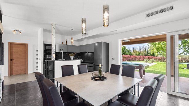 A modern kitchen with a dining area, large windows, and a view of the outdoors.