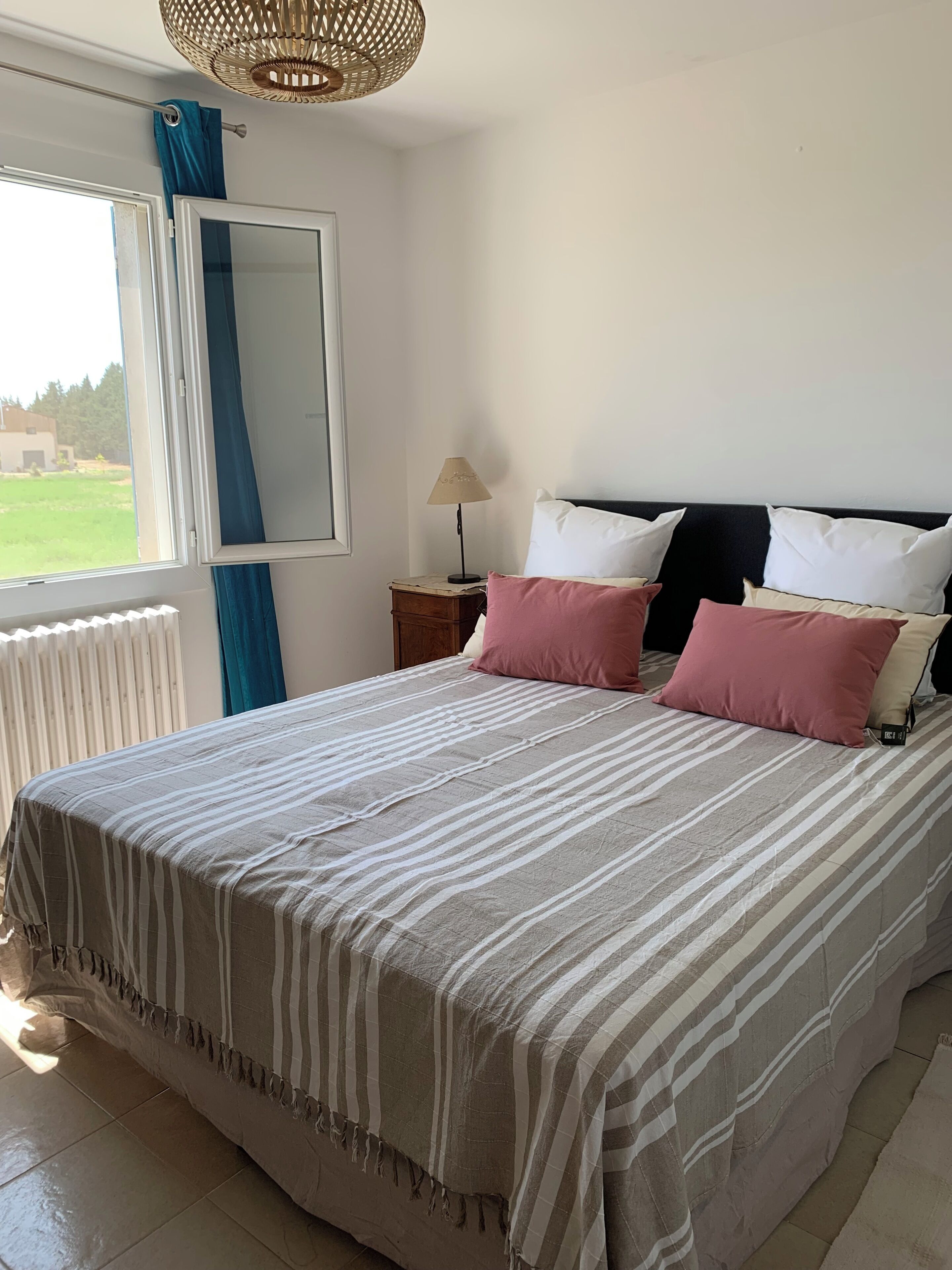 Un dormitorio con cama, mesita de noche, lámpara y ventana con cortinas.