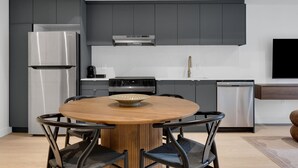 Une cuisine moderne avec des meubles de couleur sombre, des appareils en acier inoxydable et une table de salle à manger ronde en bois.