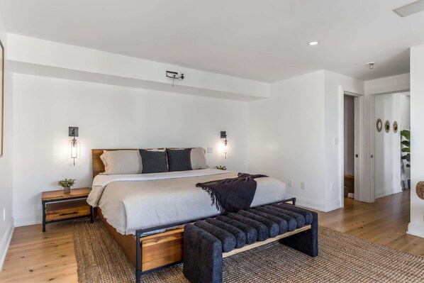 Une chambre moderne avec un grand lit, des tables de chevet, un banc et des luminaires fixés au mur.