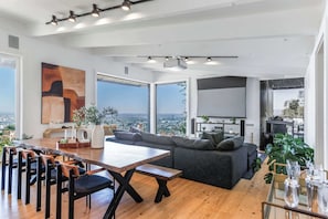 A modern living room with a large window, a dining area, and a gray sofa.