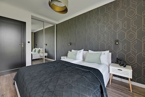 A modern bedroom with a large bed, a bedside table, a nightstand, and a mirror. - Front Park Apartments with Parking by Lion Apartments (Gdansk)