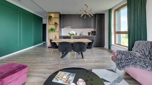 A modern living room with a dining area, a kitchen, and a large window with curtains. - Lion Apartments - Front Park (Gdansk)