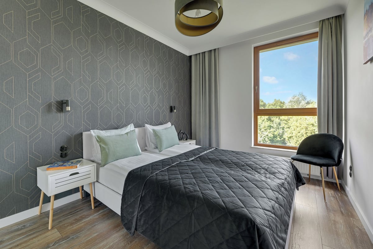 Un dormitorio moderno con una cama grande, una mesita de noche, una silla y una ventana con cortinas.