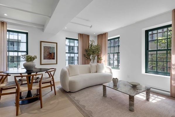 Un salon moderne avec un canapé, une table à manger, des chaises et de grandes fenêtres.