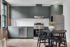 Une cuisine moderne avec des meubles gris, des appareils en acier inoxydable et un coin repas comprenant une table ronde et des chaises.