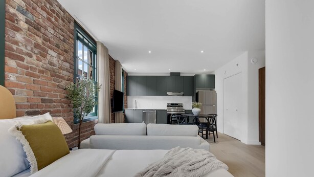 A modern room with a white sofa, a brick wall, and a kitchen area in the background. - Mercer- Studio 1Beds+Sofa bed / Free parking (Montréal)