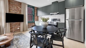 A modern kitchen with a large refrigerator, a built-in oven, and a flat-screen TV mounted on a brick wall. - Mercer- Studio 1Beds+Sofa bed / Free parking (Montréal)