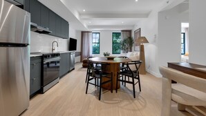 A modern kitchen with a built-in oven, a dining area with a round table and chairs, and a sofa in the living room.