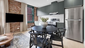 A modern kitchen with a large refrigerator, a built-in oven, and a flat-screen TV mounted on a brick wall. - Mercer- Studio 1Beds+Sofa bed / Free parking (Montréal)