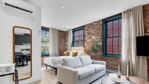 A modern bedroom with a white sofa, a bed with green and white bedding, a mirror, and a TV. - Mercer- Studio 1Beds+Sofa bed / Free parking (Montréal)