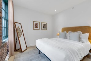 Une chambre avec un grand lit, une table de chevet avec une lampe et deux tableaux encadrés au mur.