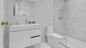 A modern bathroom with a white marble sink, a toilet, and a glass-enclosed shower.