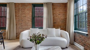 A modern living room with a white sofa, beige curtains, and a brick wall.