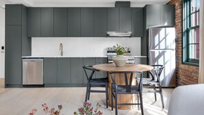 A modern kitchen with grey cabinets, a stainless steel refrigerator, and a dining area with a round wooden table and chairs.