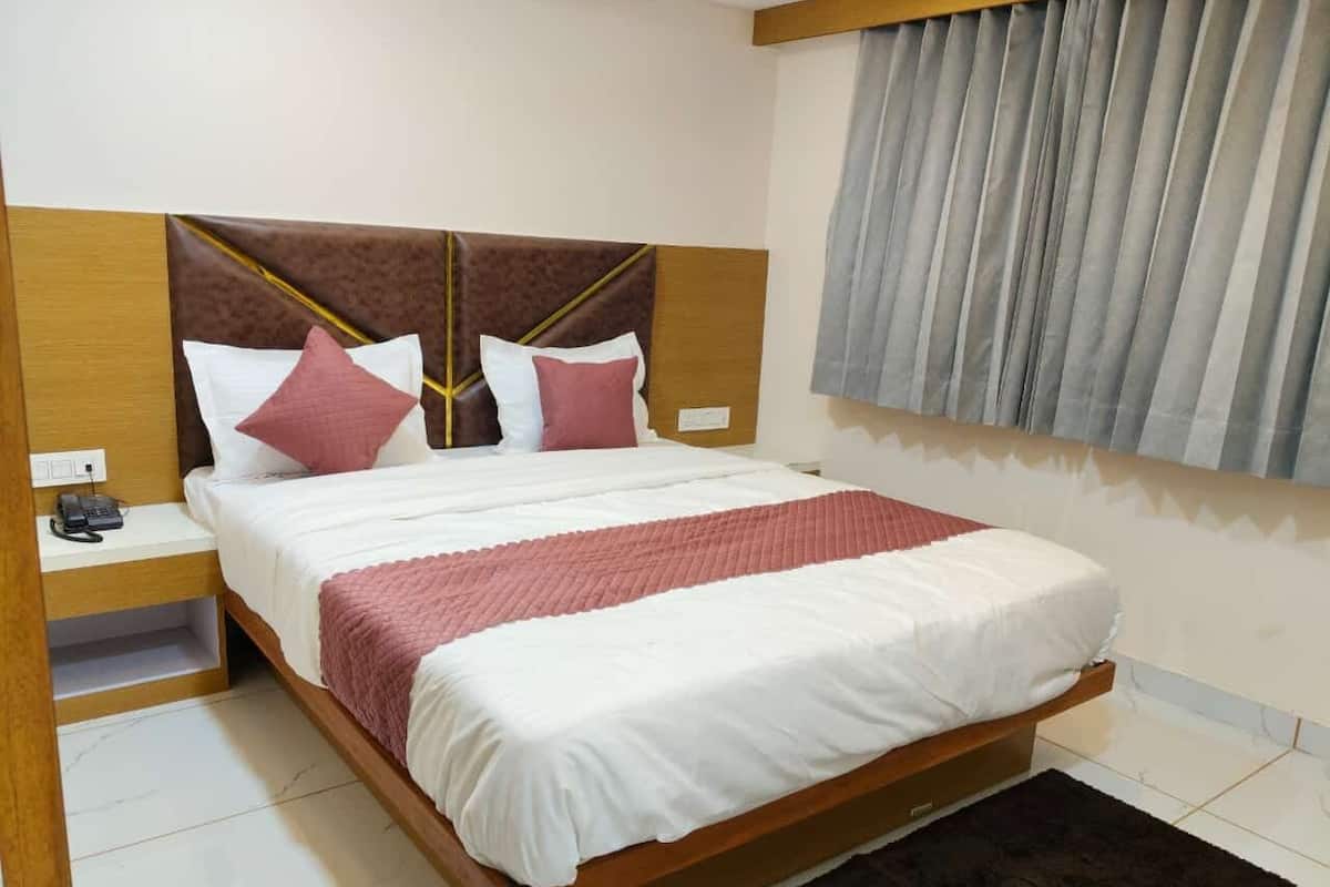 A neatly made bed with a wooden headboard, a bedside table with a phone, and a window with curtains.